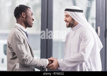 close up view of african american businessman and arabic partner smiling and shaking hands in office Stock Photo