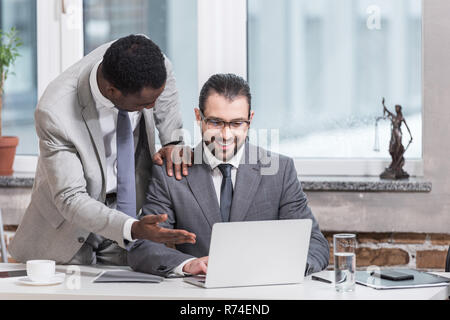african american businessman putting hand on partners shoulder and pointing at laptop in office Stock Photo
