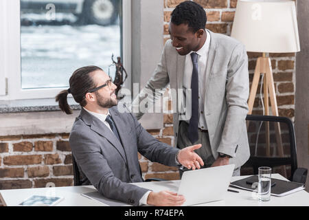 multiethnic businessmen smiling, looking at each other and talking in office Stock Photo