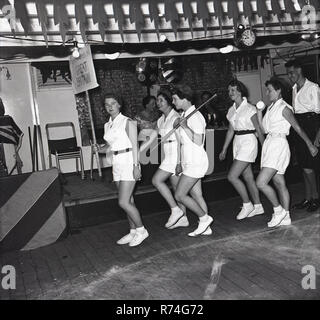 1950s, historical, fun on a crusie ship of this era, a group of ladies and one man parade below deck dressed up in sportswear as the Great Britain team in the 1955 Olympic Games in a passengers game or activity on a steamship headed for the Cape in South Africa. Stock Photo