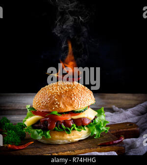 classic burger with a meatball, cheese and vegetables, on top of a bun with a sesame is a burning red chili pepper Stock Photo