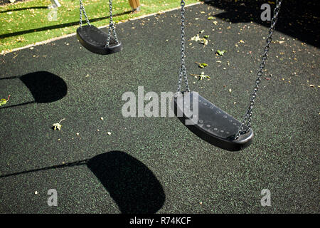 Children's swings in a playground with a rubber mat floor on a sunny day Stock Photo