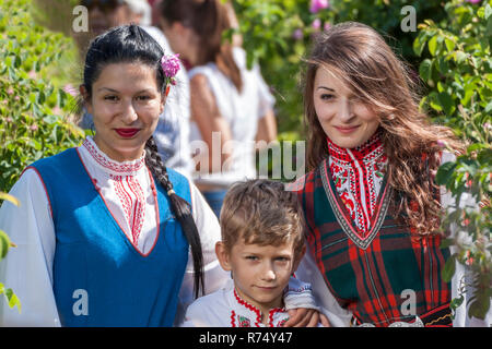 Women dressed in a Bulgarian traditional folklore costume picking roses in a garden, as part of the summer regional ritual in Rose valley, Bulgaria. Stock Photo