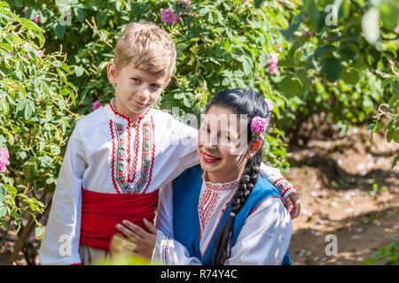 Women dressed in a Bulgarian traditional folklore costume picking roses in a garden, as part of the summer regional ritual in Rose valley, Bulgaria. Stock Photo