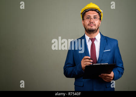 Bearded Persian businessman wearing hardhat against colored back Stock Photo