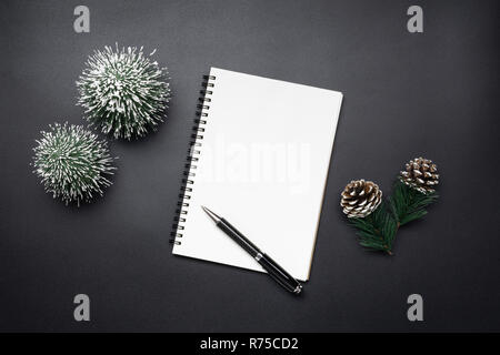 Open blank notebook, pen, pine cones and mini christmas tree in black tones. Festive Christmas and New Year concept. Stock Photo