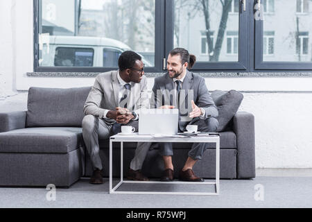 multiethnic business partners sitting on couch and having discussion Stock Photo