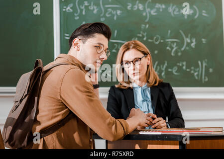Female teacher looking at young student in classroom with chalkboard on background