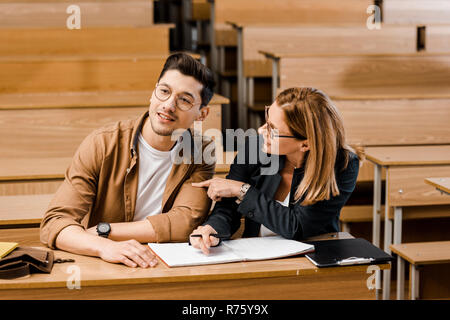 female university teacher sitting at desk with male student during exam in classroom Stock Photo