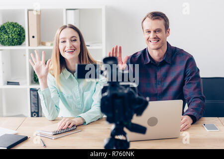 smiling journalists recording vlog and waving hands in office Stock Photo