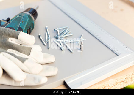 Furniture assembly. Making of kitchen cabinet. Furniture making tools placed on part of chipboard kitchen cabinet. Screws, construction ruler, protective cloves and screwdriver Stock Photo