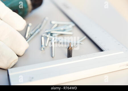 Furniture assembly. Making of kitchen cabinet. Furniture making tools placed on part of chipboard kitchen cabinet. Screws, construction ruler, protective cloves and screwdriver Stock Photo