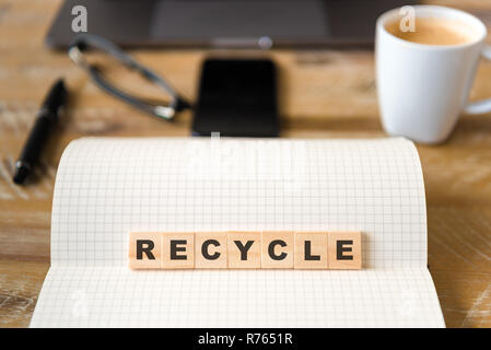 Closeup on notebook over wood table background, focus on wooden blocks with letters making Recycle text Stock Photo