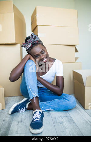 Charming young african girl standing on her knees on the floor and smiling at the camera while taking plates out of the box Stock Photo