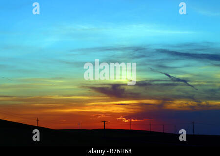 a colorful sunset behind power pylons on a field. sunset behind a power line Stock Photo