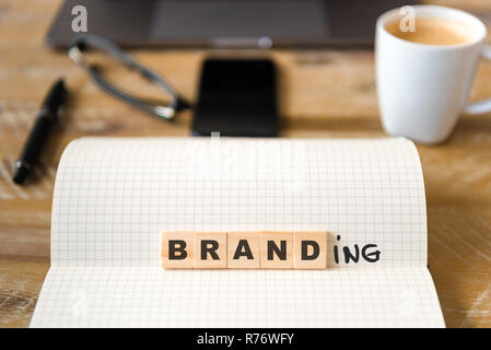 Closeup on notebook over vintage desk background, front focus on wooden blocks with letters making Branding text Stock Photo