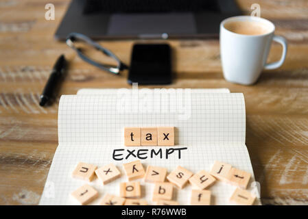 Closeup on notebook over vintage desk background, front focus on wooden blocks with letters making Tax Exempt text Stock Photo