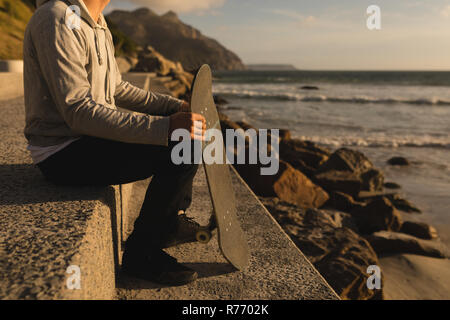 Man sitting with skateboard on the beach Stock Photo