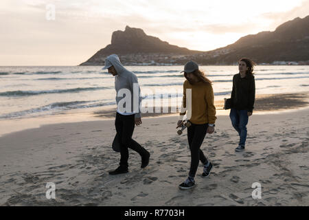 Skateboarders walking on the beach during sunset Stock Photo