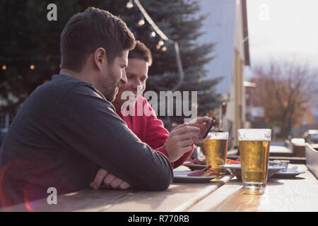 Friends discussing on mobile phone while having drinks Stock Photo