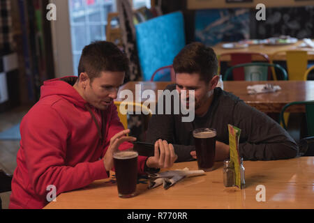 Friends discussing on mobile phone at table Stock Photo