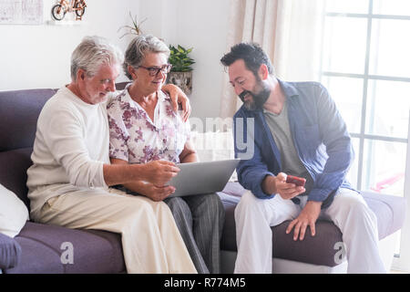 Aged family scene at home with mother father adult mature senior and son middle age with beard enjoy together the technology with laptop computer and  Stock Photo
