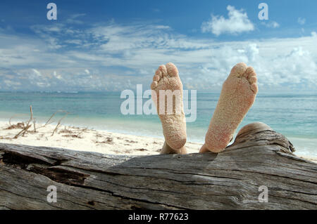 Woman lying on the beach feet up on a tree trunk, Denis Island, Seychelles Stock Photo