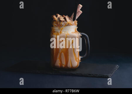 Cold chocolate and caramel milkshake in a vintage glass mason jar. Dark background with copy space for a menu. Stock Photo