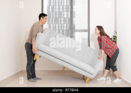 Smiling couple carrying modern chair together placing furniture moving into new home, young family discussing house improvement interior design while  Stock Photo