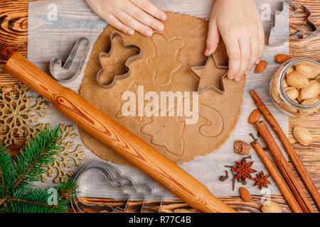 Baby's hands makes traditional gingerbread. Spices on the table-anise, cardamom, cinnamon, cloves, nutmeg, almonds. Raw dough and clippers in the form Stock Photo