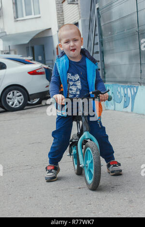 Little boy riding a balance bike along the path in the inner court on a sunny summer day Stock Photo