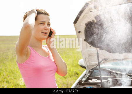 Upset Young Woman Looking For Assistance On Cellphone After Car Breakdown Stock Photo