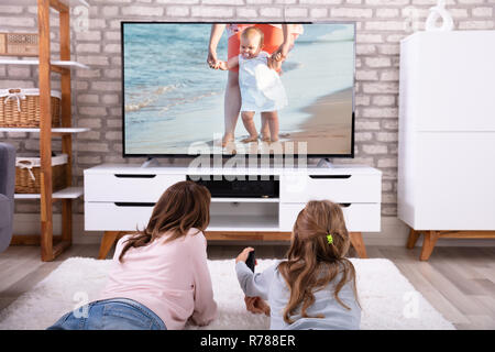 Mother And Daughter Lying On Carpet Watching Television At Home Stock Photo