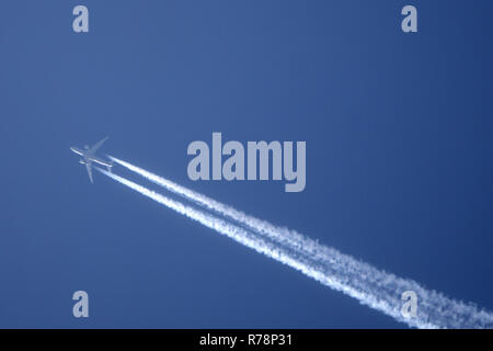 White trace of plane across the blue sky. Jet airplane is flying high Stock Photo