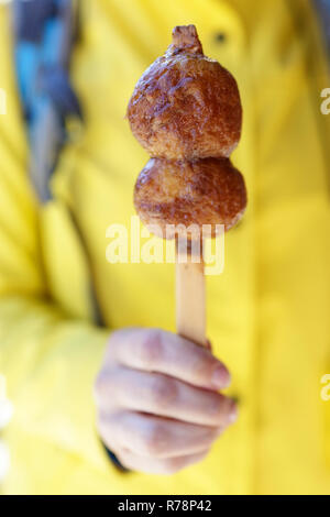 Woman in yellow jacket holding mochi balls on a stick with glazing, JApan, Tsumago Juku, Honshu Stock Photo