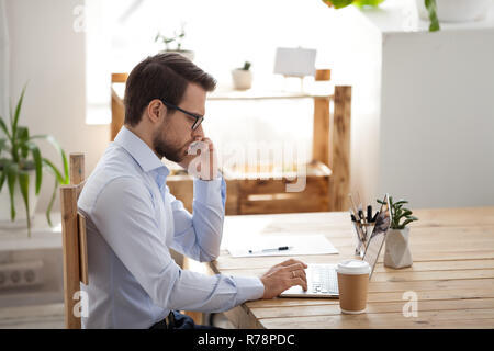 Serious male employee talking on phone using laptop Stock Photo