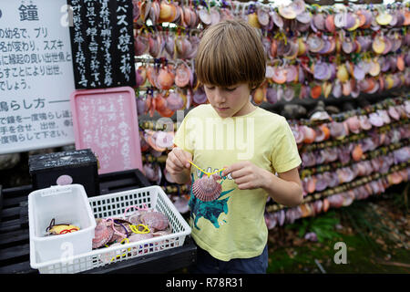 Young western boy hanging a shell on the wall of wishes display, JApan Stock Photo