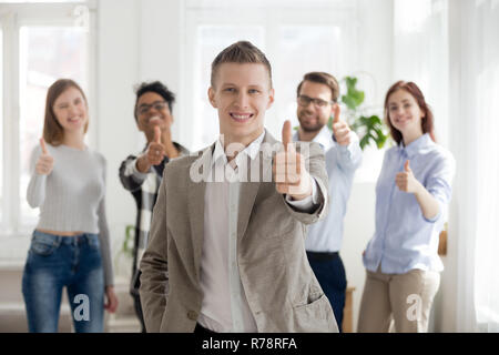 Smiling male employee with diverse team show thumbs up Stock Photo