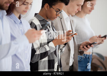 Diverse young people standing in row using smartphones  Stock Photo