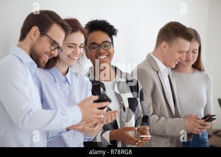 Happy diverse young people stand in queue using smartphones Stock Photo