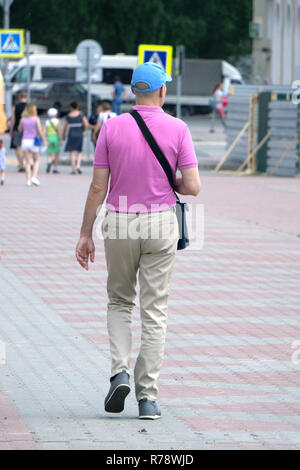 Closeup photo of man in beige tshirt standing isolated on pink background looking attentively at screen of cellphone, browsing web pages and smiling n Stock Photo