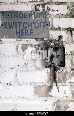 Old electricity switch box on a wall, with a sign saying "petrol pump switch off here", inside an abandoned factory in North East England, UK Stock Photo