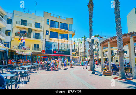 BUGIBBA, MALTA - JUNE 14, 2018: Bay Square, located on the coast, is the main shopping and gourmet area with stores, cafes, bars and the benches under Stock Photo
