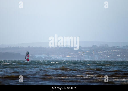 A single windsurfer on rough sees with the hills of the Isle of Wight in the background Stock Photo