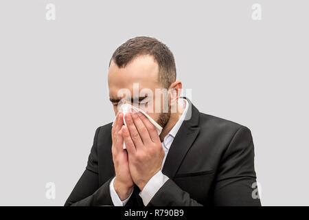 Young man sneez into white tissue. He keeps eyes closed. Young man is sick. Isolated on white background. Stock Photo