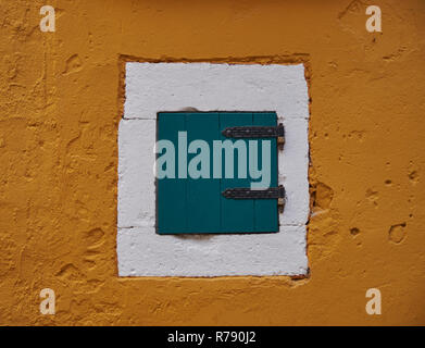 Minimalist wall capture, a single green shutter in a white frame on an ocre wall. Stock Photo
