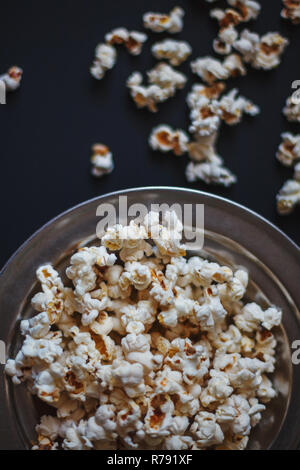 Top view of popcorn in a metallic plate on a matte black surface. Tasty source of dietary fiber. Stock Photo