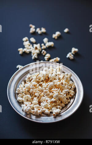 Tasty source of dietary fiber. Popcorn in a metallic plate on a dark painted matte surface. Shallow depth of field. Stock Photo