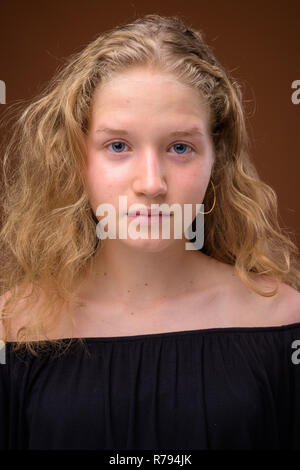 Face of young beautiful blonde teenage girl against brown background Stock Photo