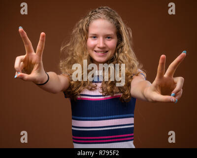 Young beautiful blonde teenage girl smiling and making peace sign gesture Stock Photo